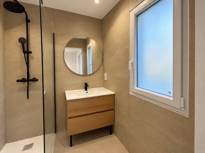Salle de bain beige avec douche noire et miroir rond
